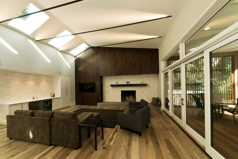 Exemple d'une salle de séjour tendance fermée avec un bar de salon, un mur blanc, un sol en bois brun et un téléviseur fixé au mur.