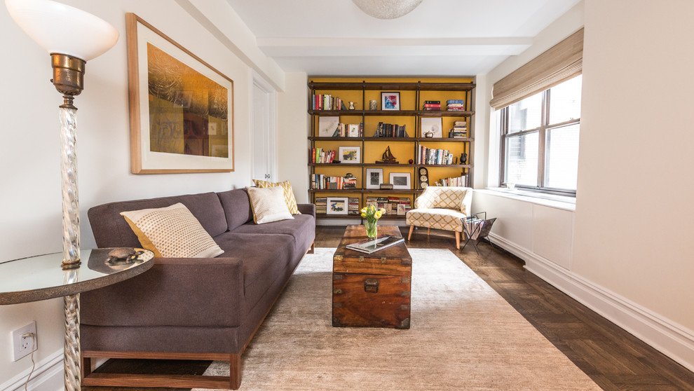 Imagen de sala de estar con biblioteca cerrada minimalista con paredes blancas y suelo de madera oscura