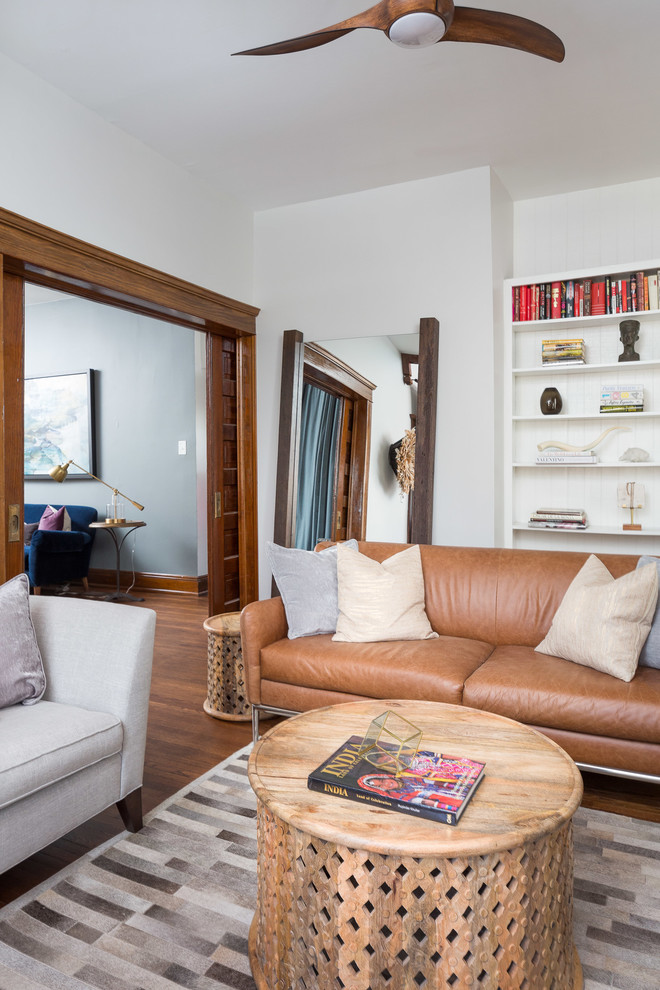 Imagen de sala de estar con biblioteca cerrada tradicional renovada de tamaño medio con paredes blancas, suelo de madera en tonos medios, todas las chimeneas y marco de chimenea de ladrillo