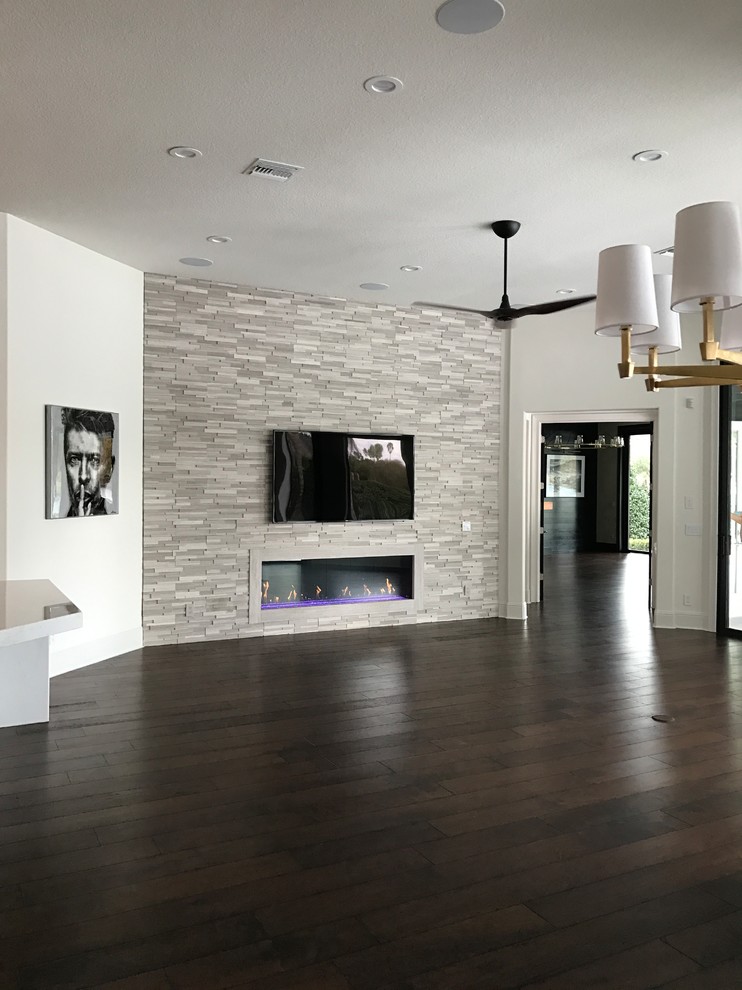 Diseño de sala de estar abierta minimalista grande con paredes blancas, suelo de madera oscura, todas las chimeneas, marco de chimenea de piedra, televisor colgado en la pared y suelo marrón