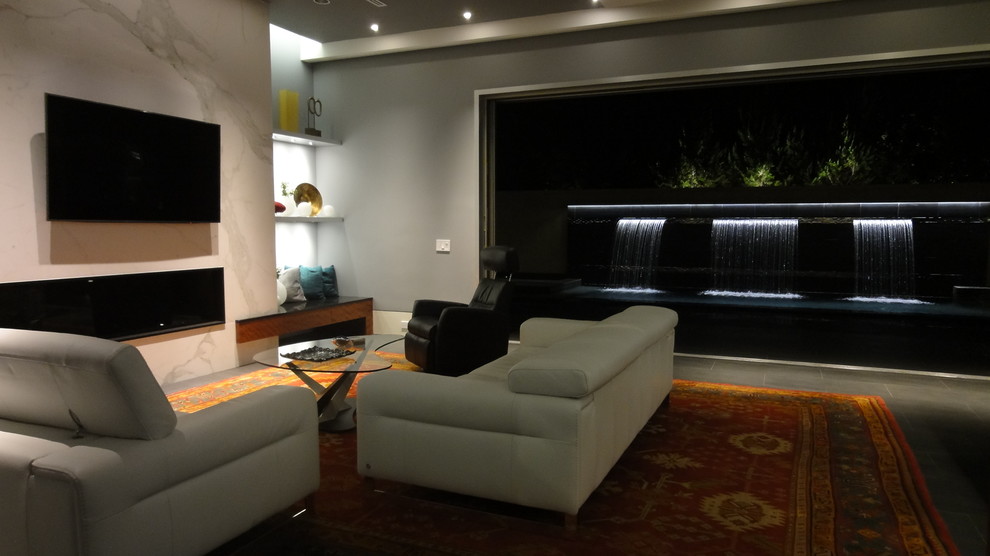Ejemplo de sala de estar abierta minimalista grande con paredes grises, suelo de baldosas de porcelana, chimenea lineal, marco de chimenea de piedra y televisor colgado en la pared