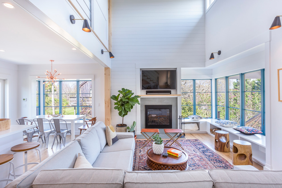 Modelo de sala de estar abierta contemporánea grande con paredes blancas, suelo de madera clara, todas las chimeneas, marco de chimenea de hormigón y televisor colgado en la pared