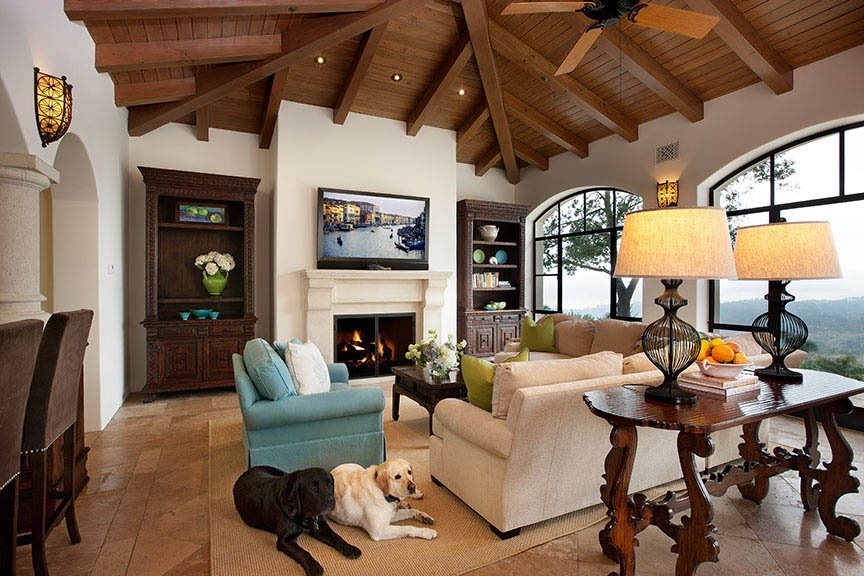 Example of a mid-sized tuscan enclosed travertine floor and beige floor family room design in Santa Barbara with white walls, a standard fireplace, a plaster fireplace and a wall-mounted tv
