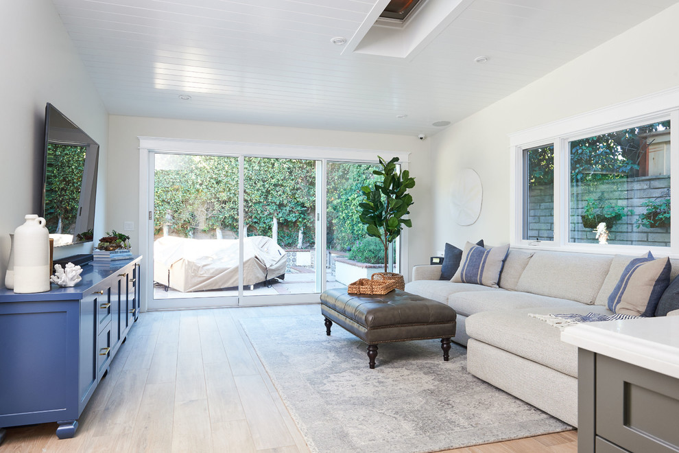 Imagen de sala de estar abierta costera grande con paredes blancas, suelo de baldosas de cerámica, televisor colgado en la pared y suelo marrón