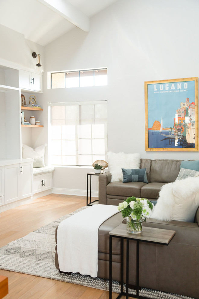 Modelo de sala de estar abierta costera grande sin chimenea con paredes grises, suelo de madera en tonos medios, pared multimedia y suelo marrón