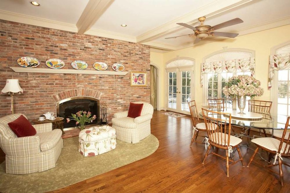 Ejemplo de sala de estar abierta tradicional de tamaño medio con paredes beige, suelo de madera en tonos medios, todas las chimeneas y marco de chimenea de ladrillo
