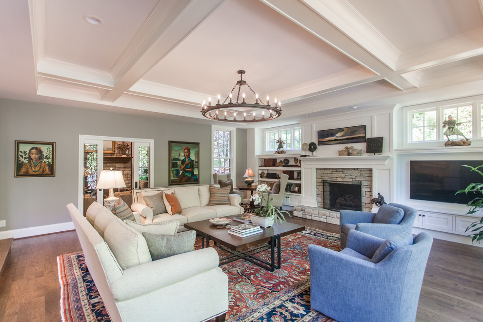 This is an example of a large classic open plan games room in Cincinnati with white walls, dark hardwood flooring, a standard fireplace, a stone fireplace surround, a wall mounted tv and brown floors.