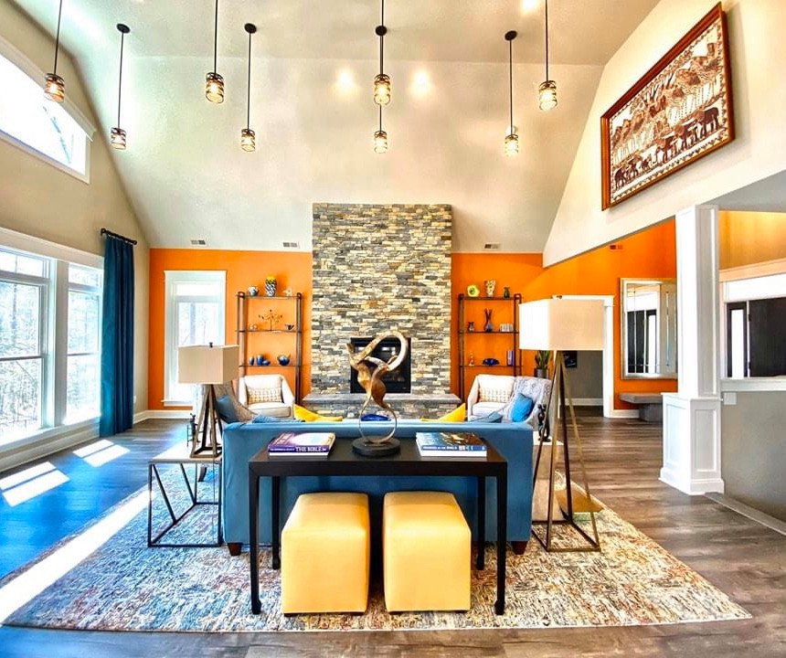 На фото: гостиная комната в современном стиле с оранжевыми стенами, полом из ламината, фасадом камина из камня, серым полом и сводчатым потолком