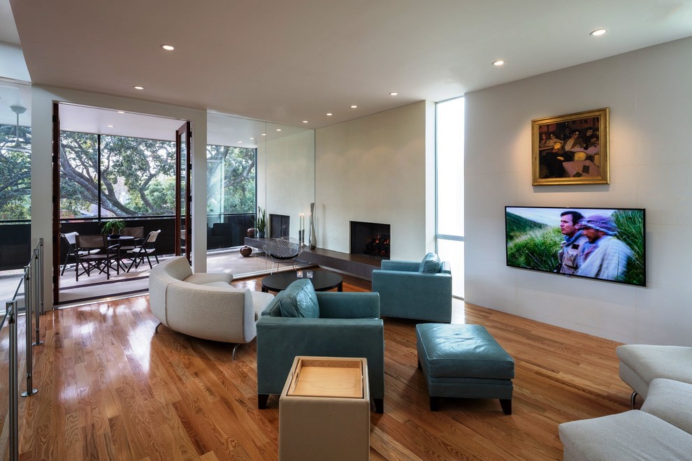 Imagen de sala de estar abierta contemporánea con suelo de madera en tonos medios y televisor colgado en la pared