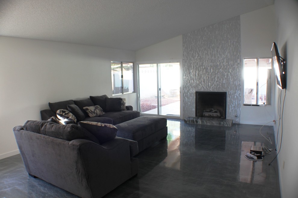 На фото: открытая гостиная комната среднего размера в современном стиле с стандартным камином, фасадом камина из плитки, серыми стенами, бетонным полом и телевизором на стене