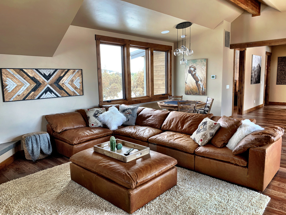 This is an example of a large rustic mezzanine games room in Other with a game room, beige walls, dark hardwood flooring, a corner fireplace, a stone fireplace surround, a built-in media unit and brown floors.