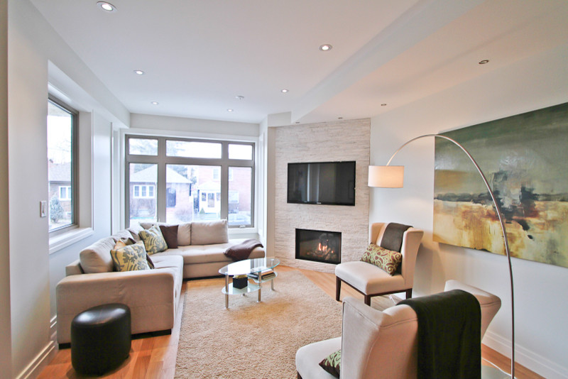 Mittelgroßes, Abgetrenntes Modernes Wohnzimmer mit grauer Wandfarbe, braunem Holzboden, Eckkamin, Kaminumrandung aus Stein, TV-Wand und braunem Boden in Toronto