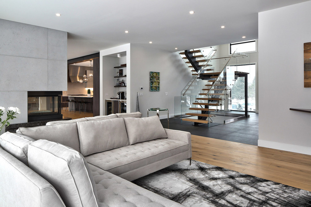 Großes, Offenes Modernes Wohnzimmer mit grauer Wandfarbe, hellem Holzboden, Kaminumrandung aus Beton, TV-Wand, Tunnelkamin und beigem Boden in Toronto
