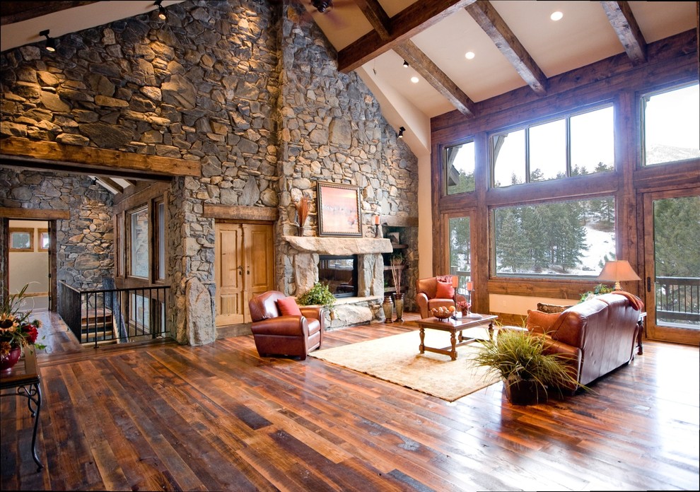 Ejemplo de sala de estar abierta rural extra grande con suelo de madera en tonos medios, todas las chimeneas y marco de chimenea de piedra