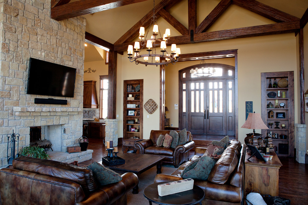 Large rustic open plan games room in Dallas with yellow walls, dark hardwood flooring, a two-sided fireplace, a stone fireplace surround, a wall mounted tv and brown floors.