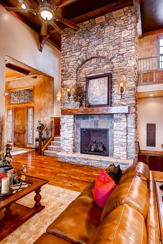 Großes, Offenes Uriges Wohnzimmer mit beiger Wandfarbe, braunem Holzboden, Kamin und Kaminumrandung aus Stein in Denver