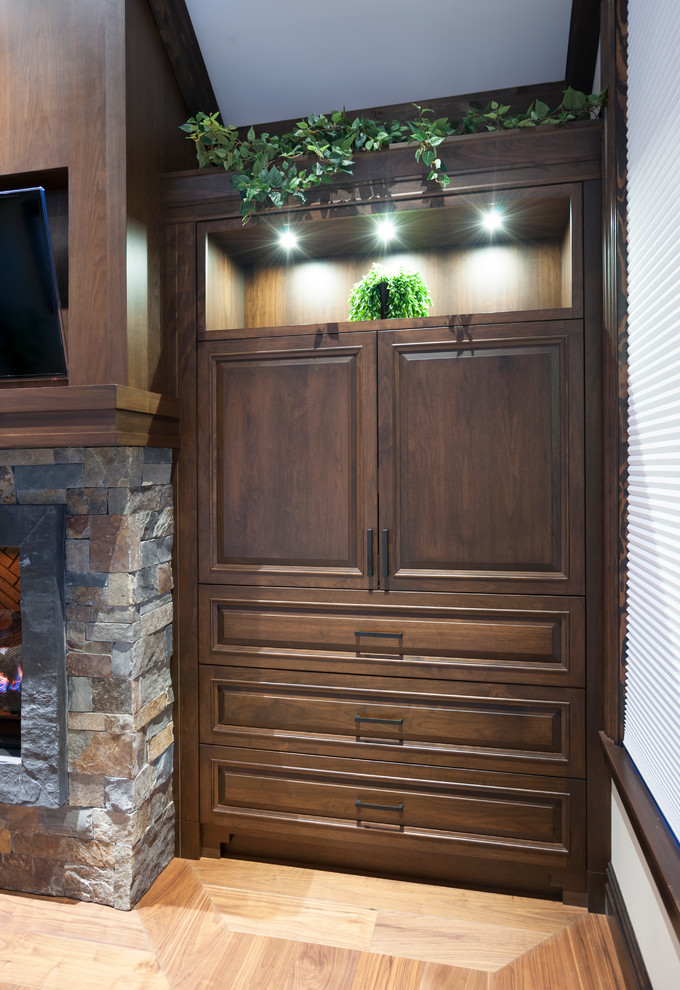 Medium sized rustic enclosed games room in Calgary with beige walls, medium hardwood flooring, a standard fireplace, a stone fireplace surround, a built-in media unit and beige floors.