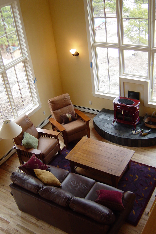 Modelo de sala de estar abierta actual pequeña sin televisor con paredes amarillas, suelo de madera en tonos medios, estufa de leña y marco de chimenea de piedra