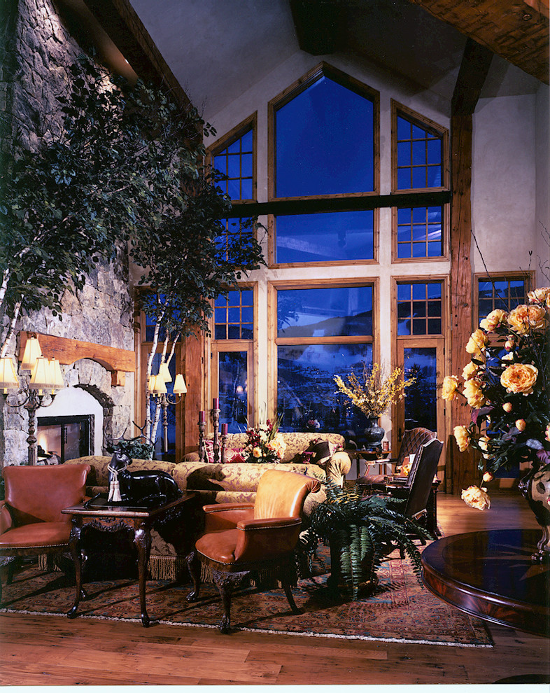 Modelo de sala de estar abierta rural extra grande con suelo de madera en tonos medios, todas las chimeneas y marco de chimenea de piedra