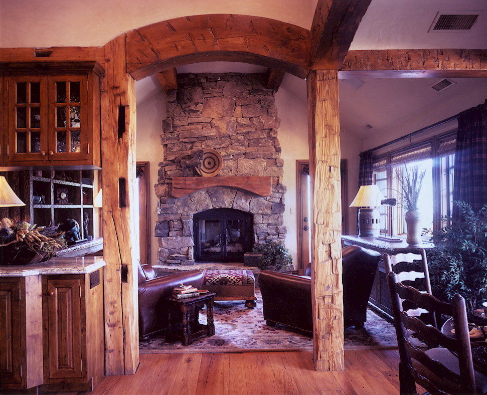 Modelo de sala de estar abierta rural extra grande con suelo de madera clara, todas las chimeneas y marco de chimenea de piedra