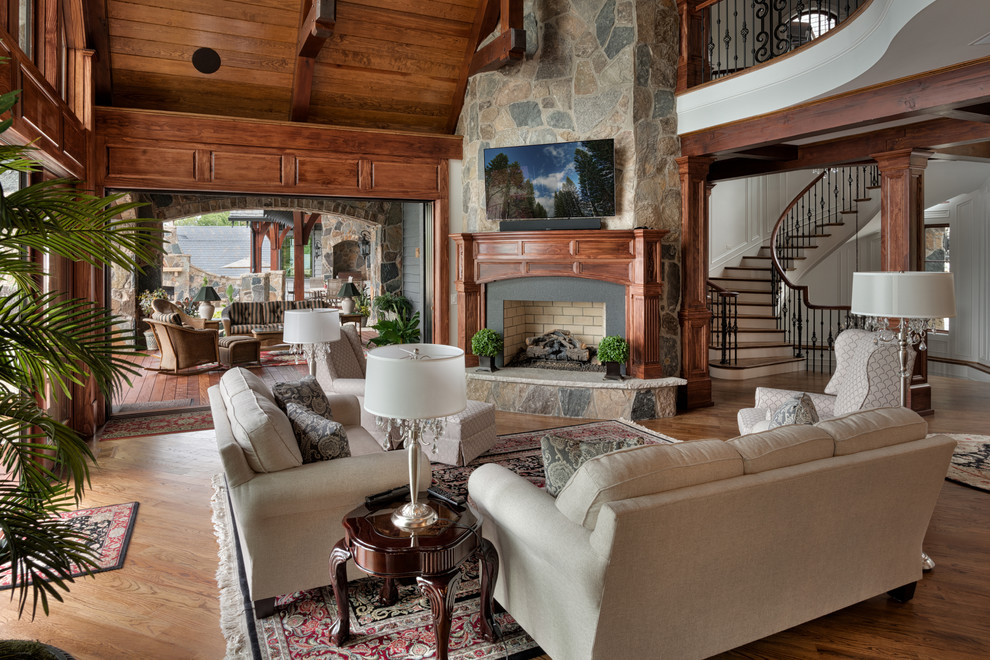 Imagen de sala de estar abierta tradicional con suelo de madera oscura, todas las chimeneas, marco de chimenea de piedra y televisor colgado en la pared