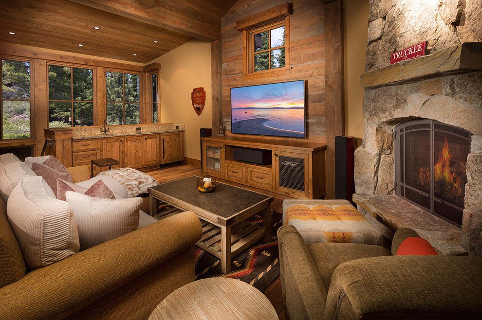 Foto de sala de estar con barra de bar cerrada rural de tamaño medio con paredes beige, suelo de madera en tonos medios, todas las chimeneas, marco de chimenea de piedra y televisor colgado en la pared