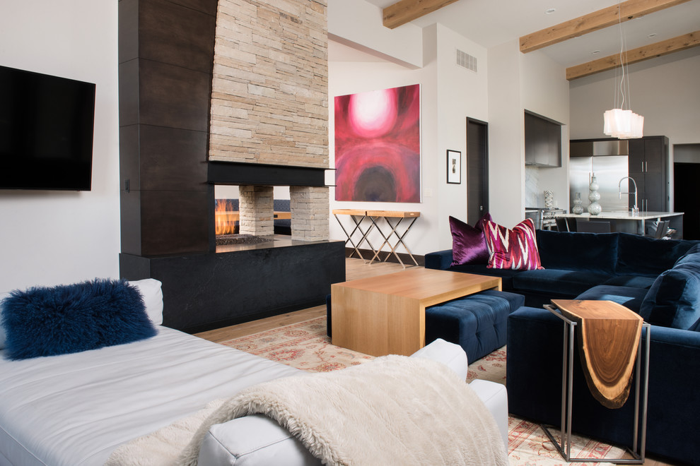 На фото: открытая гостиная комната в современном стиле с белыми стенами, двусторонним камином, телевизором на стене и ковром на полу с