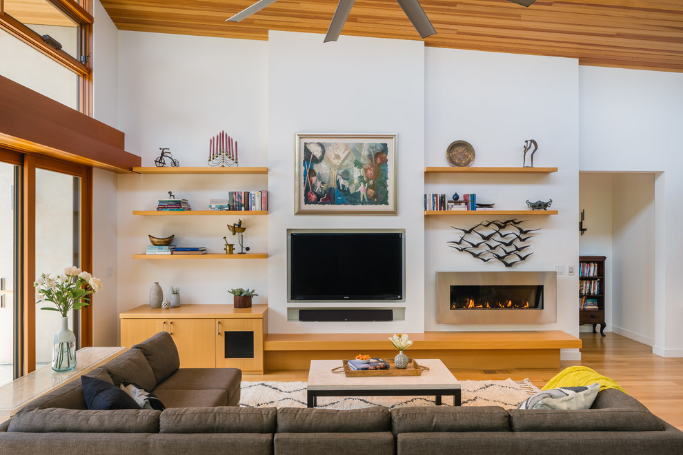 Diseño de sala de estar abierta contemporánea con paredes blancas, suelo de madera clara, chimenea lineal y televisor colgado en la pared
