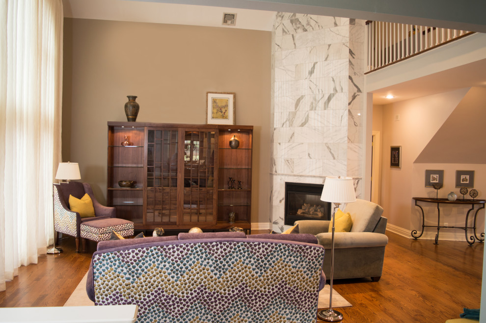 Cette photo montre une grande salle de séjour chic ouverte avec un sol en bois brun, une cheminée d'angle, un manteau de cheminée en pierre, un téléviseur dissimulé, un mur gris et un sol marron.