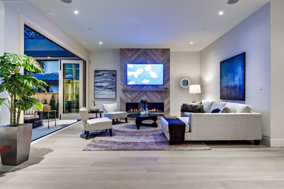 Offenes Modernes Wohnzimmer mit grauer Wandfarbe, hellem Holzboden, Kamin, gefliester Kaminumrandung und TV-Wand in Vancouver