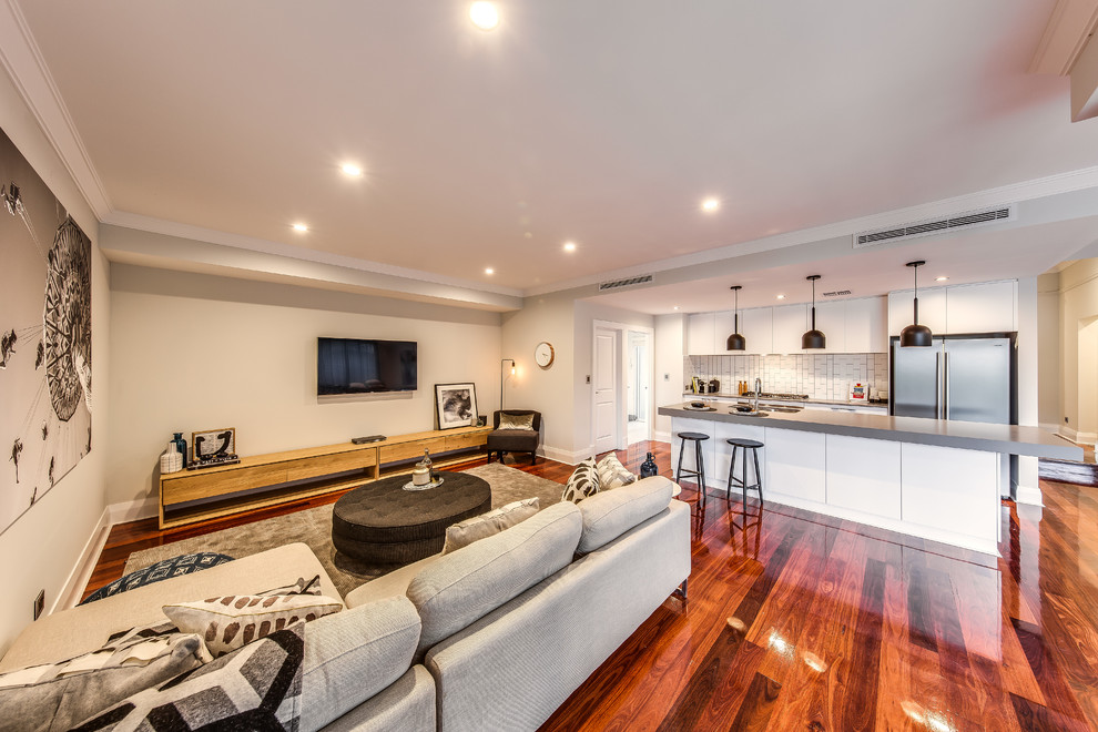 Imagen de sala de estar abierta contemporánea grande con paredes grises, suelo de madera en tonos medios y televisor colgado en la pared