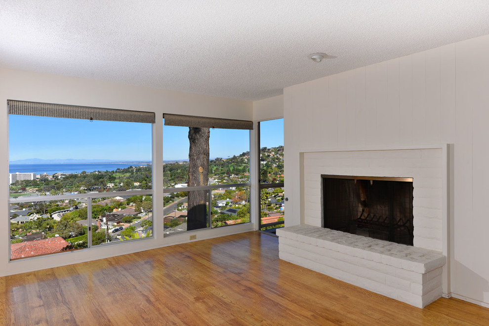 Photo of a medium sized midcentury open plan games room in San Diego with white walls, light hardwood flooring, a standard fireplace, a brick fireplace surround and no tv.