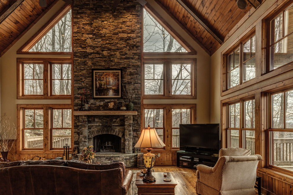 Large mountain style medium tone wood floor family room photo in Charlotte with beige walls, a standard fireplace, a stone fireplace and a tv stand