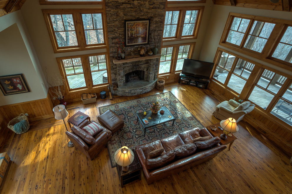Großes Rustikales Wohnzimmer im Loft-Stil mit beiger Wandfarbe, braunem Holzboden, Kamin, Kaminumrandung aus Stein und freistehendem TV in Charlotte