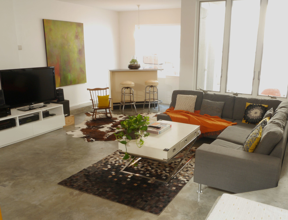 Modelo de sala de estar cerrada bohemia grande con paredes blancas, suelo de cemento y televisor independiente