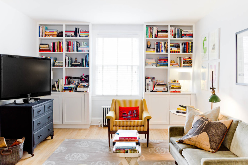 На фото: гостиная комната в стиле фьюжн с с книжными шкафами и полками, белыми стенами, светлым паркетным полом и отдельно стоящим телевизором с