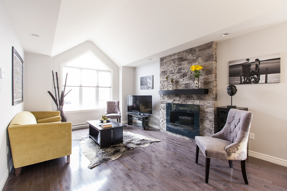 Réalisation d'une salle de séjour design avec un mur gris, un sol en bois brun, une cheminée standard, un manteau de cheminée en pierre et un téléviseur indépendant.