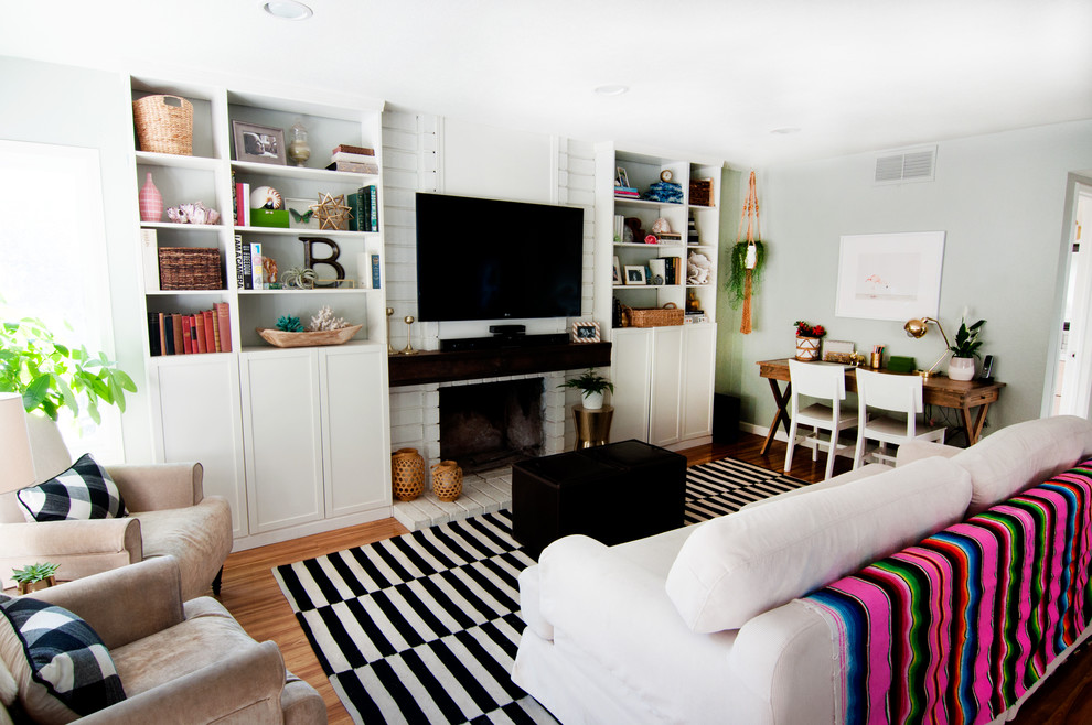 Ejemplo de sala de estar abierta bohemia de tamaño medio con paredes grises, todas las chimeneas, marco de chimenea de ladrillo y televisor colgado en la pared