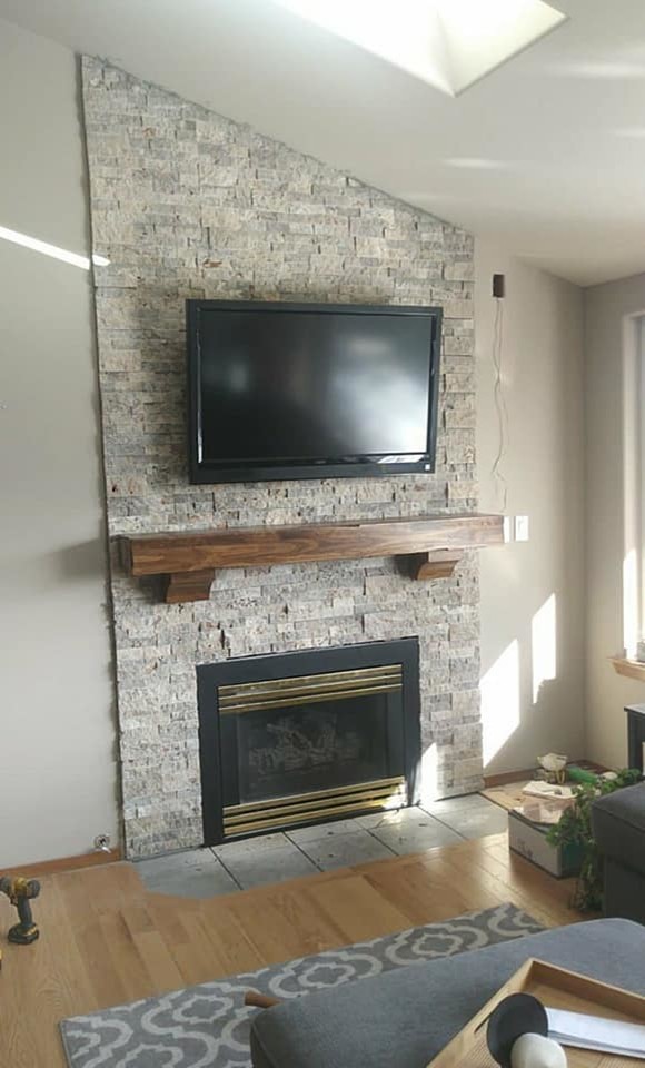 Aménagement d'une salle de séjour craftsman avec un mur blanc, un sol en bois brun, une cheminée standard, un manteau de cheminée en pierre, un téléviseur fixé au mur et un sol marron.