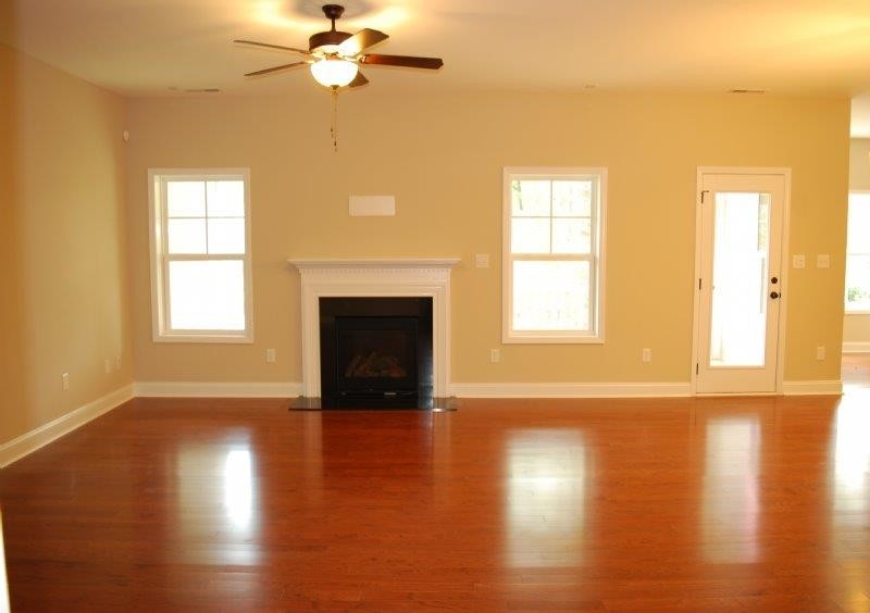 Cette photo montre une salle de séjour chic de taille moyenne et ouverte avec un sol en bois brun, une cheminée standard, un mur beige, un manteau de cheminée en plâtre et un téléviseur fixé au mur.