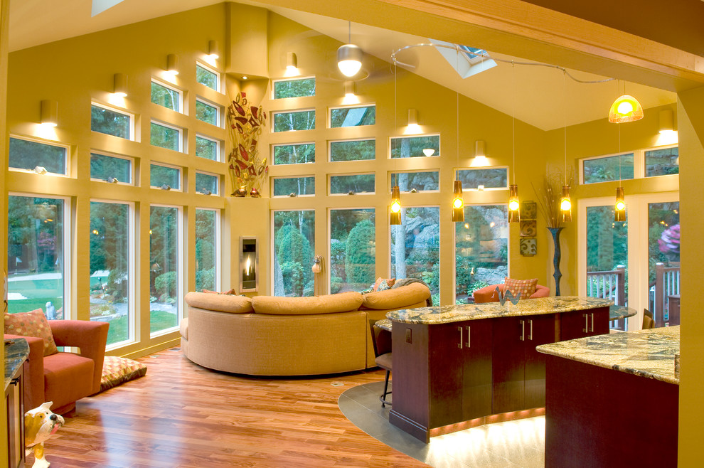 Modelo de sala de estar abierta contemporánea extra grande con chimenea de esquina, paredes amarillas y suelo de madera clara