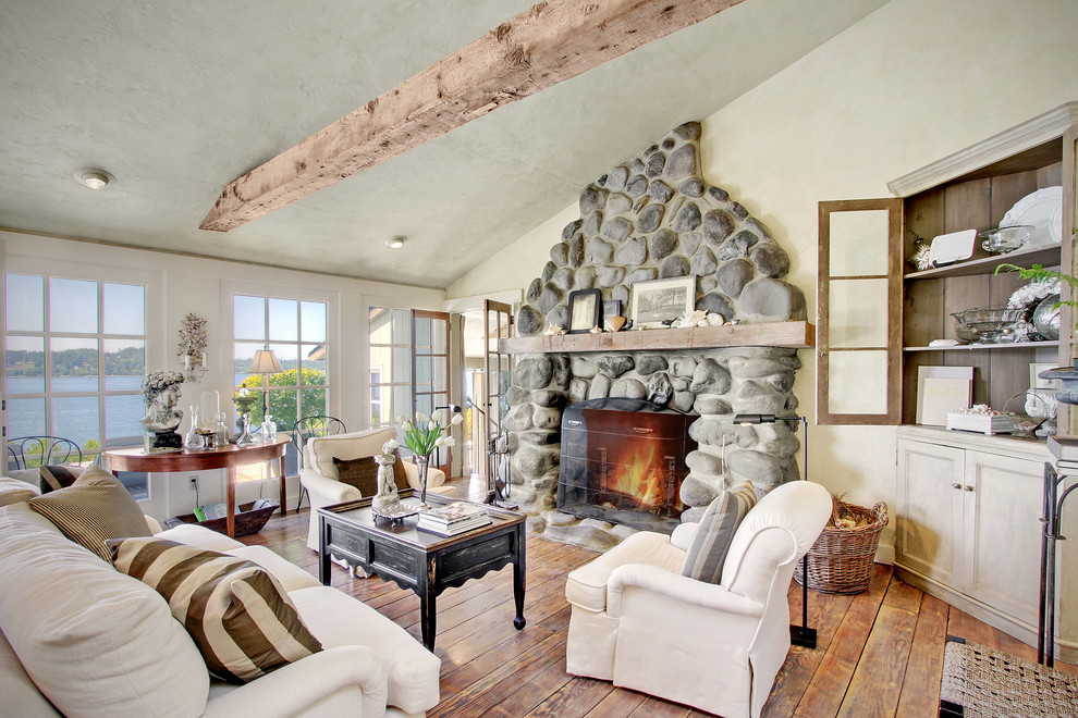 Imagen de sala de estar marinera con paredes beige, suelo de madera en tonos medios, todas las chimeneas y marco de chimenea de piedra