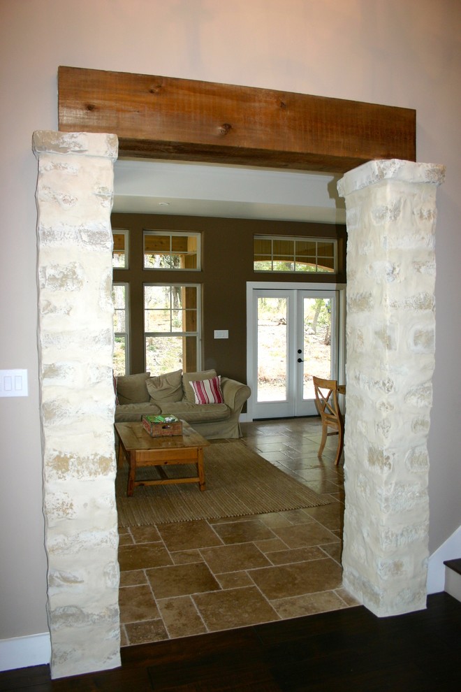 Aménagement d'une grande salle de séjour campagne ouverte avec un sol en travertin, une cheminée standard, un sol beige, un manteau de cheminée en pierre et un mur marron.