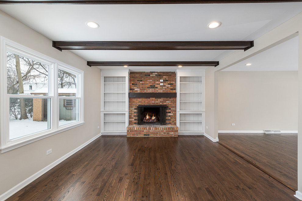 This is an example of a classic open plan games room in Chicago with beige walls, dark hardwood flooring, a standard fireplace, a brick fireplace surround and brown floors.