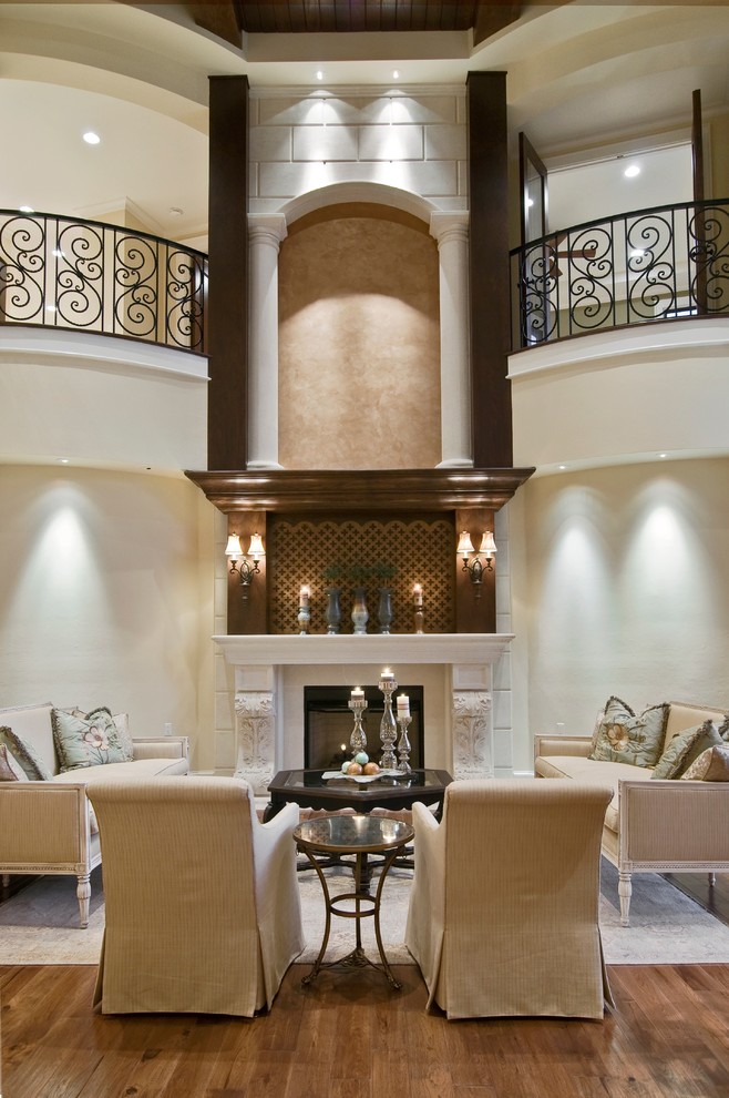 На фото: огромная открытая гостиная комната в средиземноморском стиле с бежевыми стенами, темным паркетным полом, стандартным камином и фасадом камина из камня без телевизора