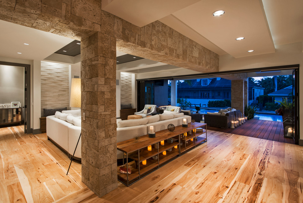 Diseño de sala de estar abierta minimalista grande con paredes blancas, suelo de madera clara y televisor colgado en la pared
