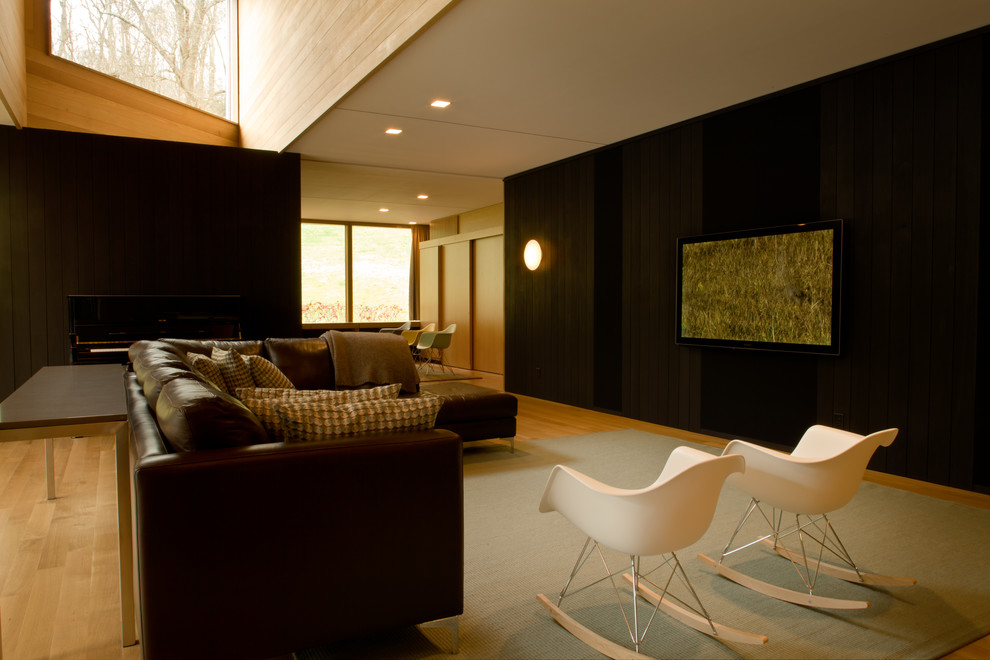 На фото: большая открытая гостиная комната в стиле модернизм с черными стенами, светлым паркетным полом, телевизором на стене и коричневым полом без камина с