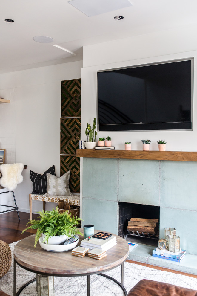 This is an example of a medium sized eclectic open plan games room in San Francisco with white walls, dark hardwood flooring, a standard fireplace, a concrete fireplace surround, a wall mounted tv and brown floors.