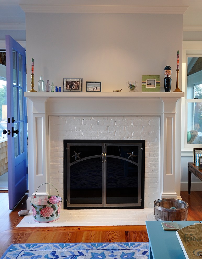 Imagen de sala de estar marinera con paredes azules, suelo de madera clara, todas las chimeneas y marco de chimenea de madera