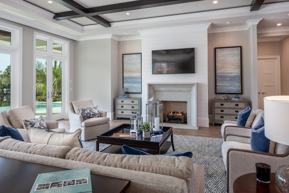 Идея дизайна: открытая гостиная комната в стиле неоклассика (современная классика) с серыми стенами, светлым паркетным полом, стандартным камином, телевизором на стене и ковром на полу